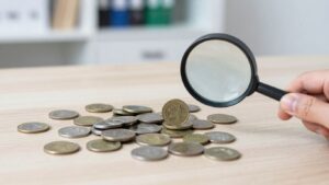 Person inspecting coins with a magnifying glass.